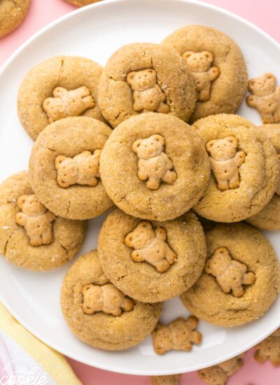 Overhead shot of teddy graham peanut butter cookies on a white plate, and a pink background.