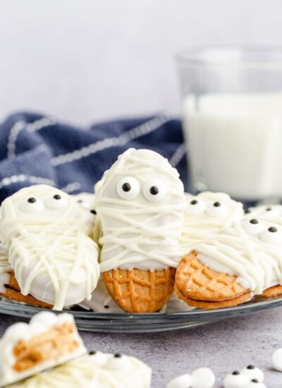 Nutter butter mummies on a plate, with a glass of milk in the background