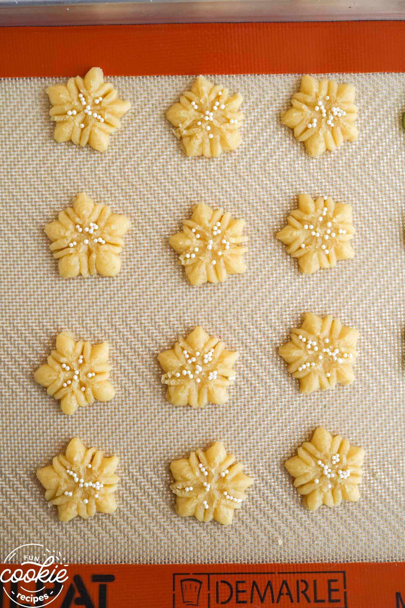 Overhead shot of snowflake spritz cookies on a silicone mat before baking