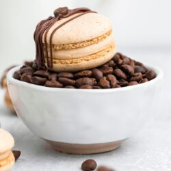 A coffee macaron placed on a small bowl filled with coffee beans