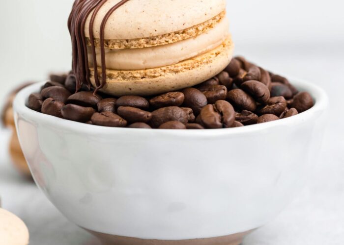 A coffee macaron placed on a small bowl filled with coffee beans
