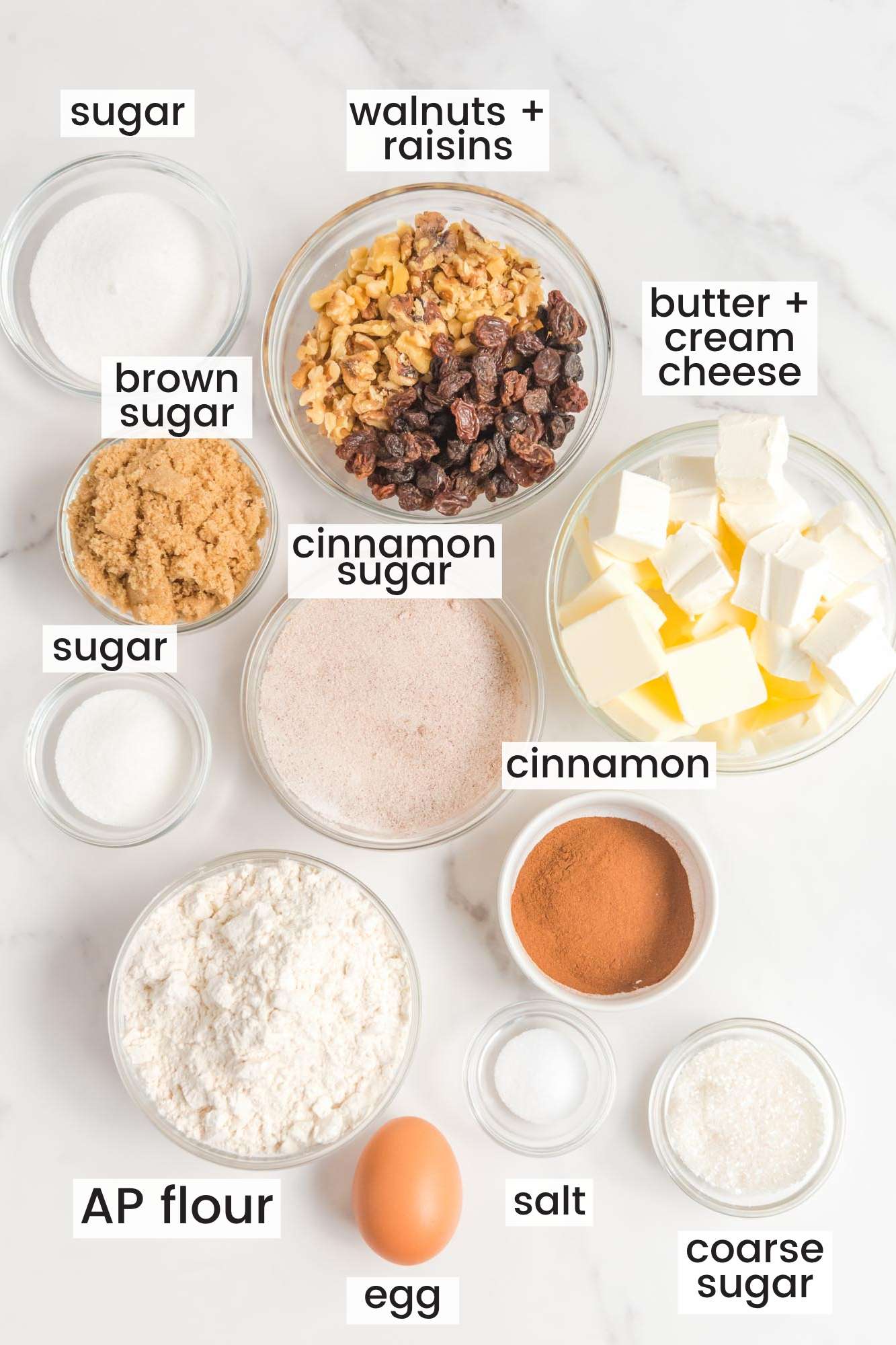 The ingredients you need to make rugelach cookies, all in small bowls, arranged on a counter. Each ingredient in labeled with a text box.
