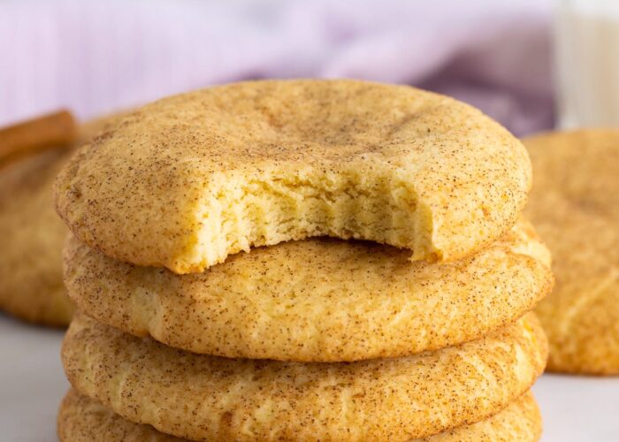 four large snickerdoodle cookies stacked on top of each other. The one on on top has a bite taken out of it.