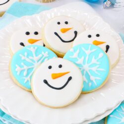 Snowman and snowflake sugar cookies on a white plate, with blue tea towels