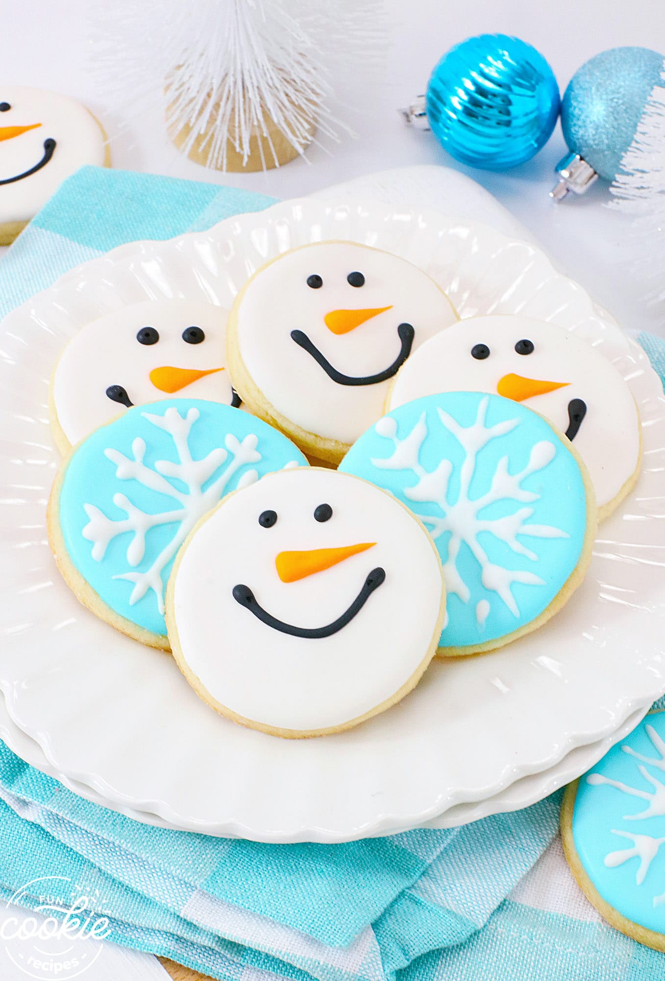 Snowman and snowflake sugar cookies on a white plate, with blue tea towels
