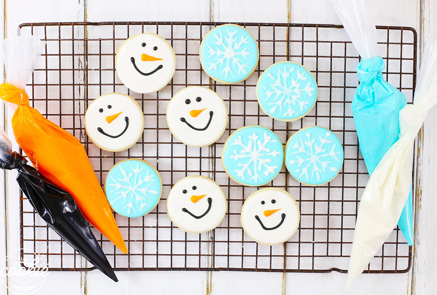 Overhead shot of snowman and snowflake sugar cookies on a wire rack with icing in pipping bags