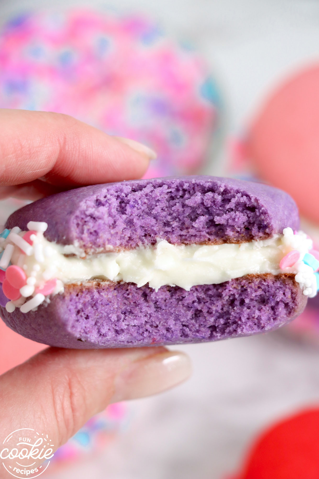 a purple whoopie pie, bitten into to show the filling, held by a hand.