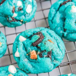 Blue cookies on a wire rack with white chocolate chips and crushed oreos and chocolate chip cookies mixed in.
