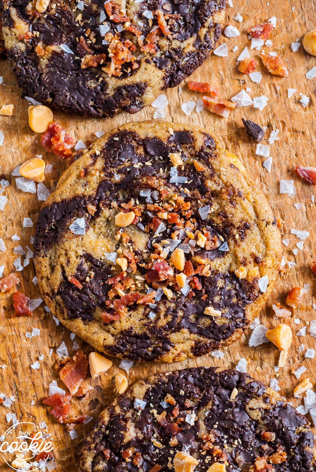a wooden board holding chocolate chunk cookies with bacon and salt on top.