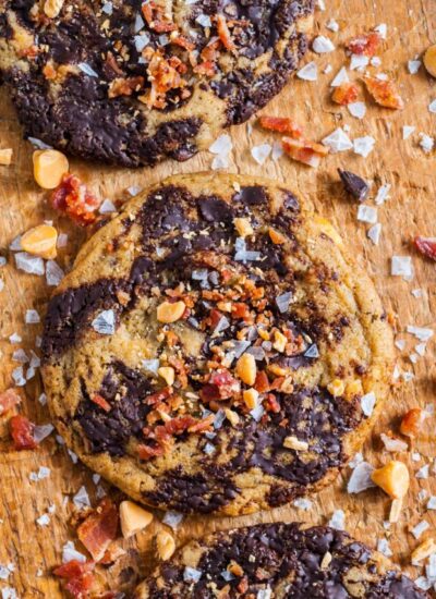 a wooden board holding chocolate chunk cookies with bacon and salt on top.