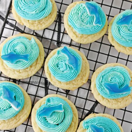 sugar cookies with blue frosting and gummy sharks, on a wire rack.