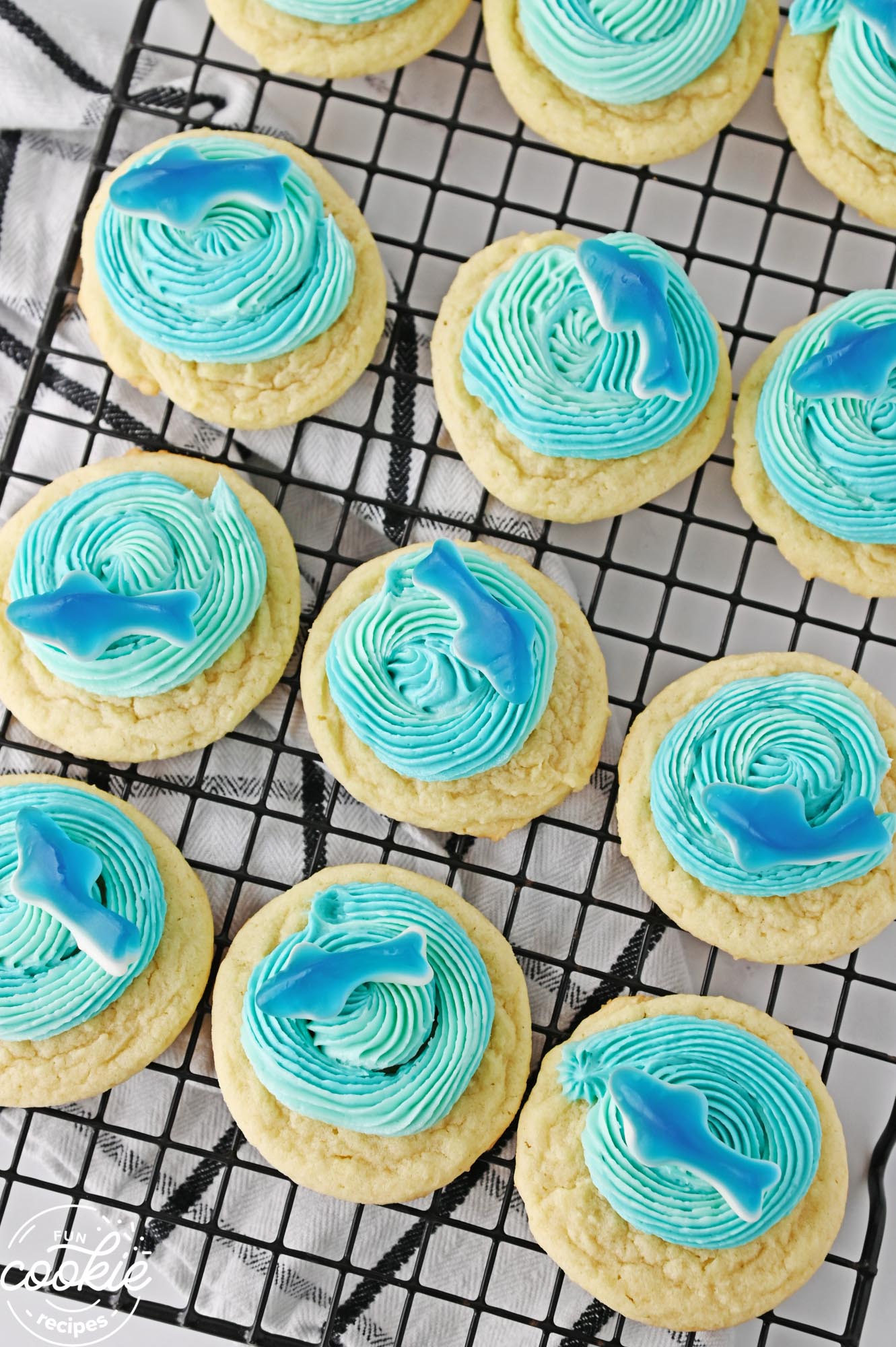 sugar cookies with blue frosting and gummy sharks, on a wire rack. 