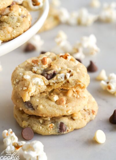 Three popcorn cookies stacked on top of each other, a bite is taken from the top one. Popcorn is strewn around.