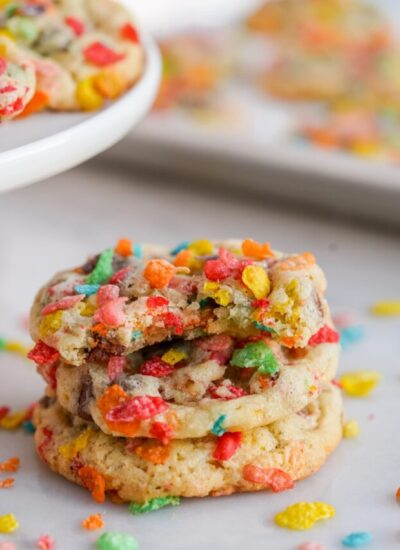 Three cookies with fruity pebbles stacked. The top cookie has a bite taken.