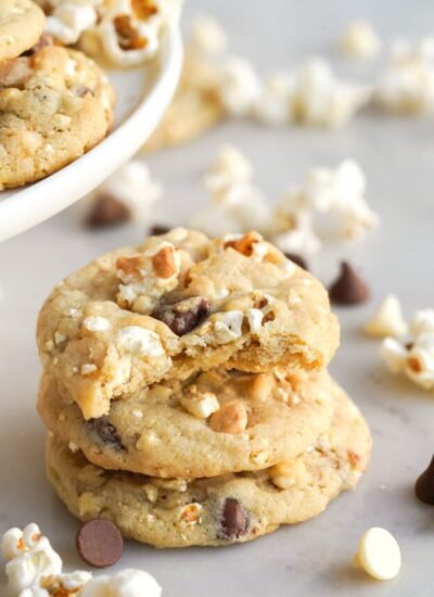Three popcorn cookies stacked on top of each other, a bite is taken from the top one. Popcorn is strewn around.