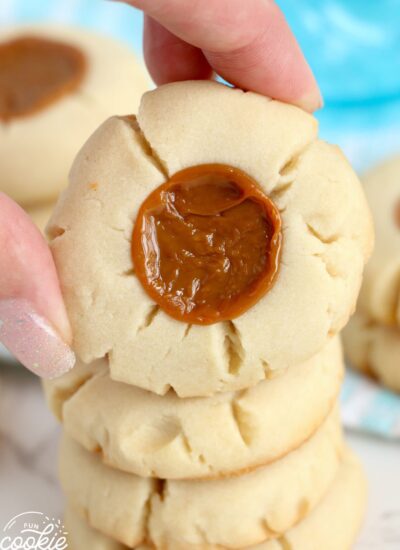 Holding a dulche de leche cookie with a hand, over stacked cookies.