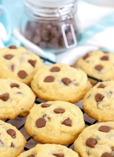 homemade chocolate chip cookies on a black wire rack. In the background is a small jar of chocolate chips.