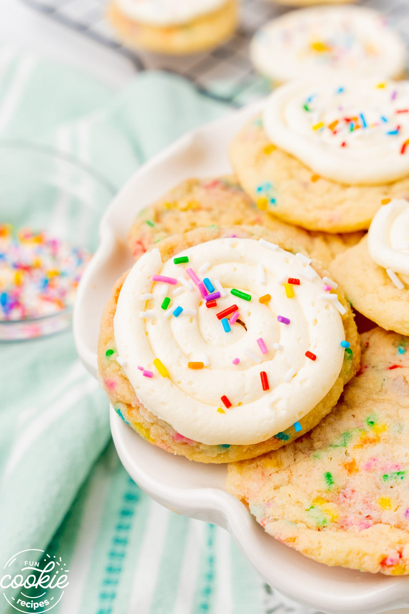 a plate of sugar cookies. The ones on top are covered with buttercream frosting and colorful sprinkles. 