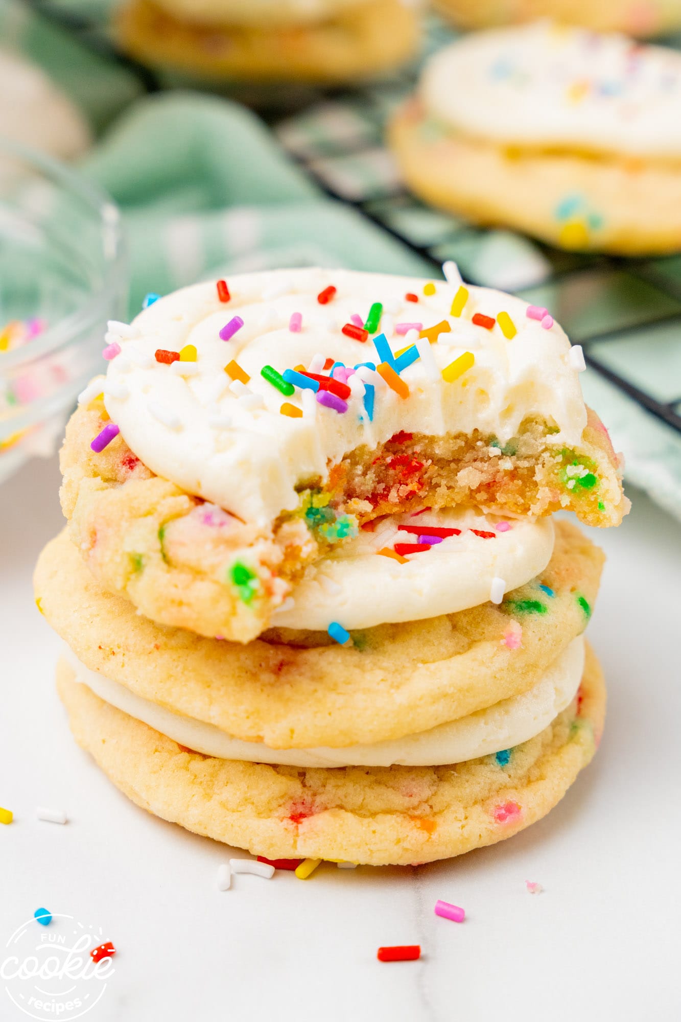 a stack of three frosted birthday cake cookies. The top one has been bitten into to show the sprinkles inside.