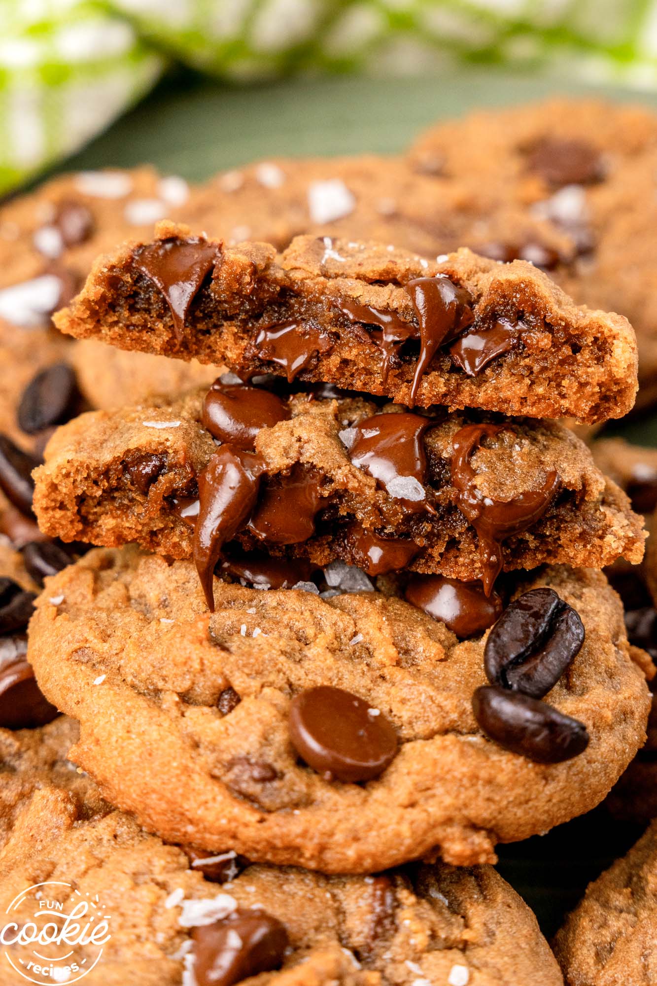 closeup of a pile of coffee cookies. One is broken in half to reveal melty chocolate chips inside.