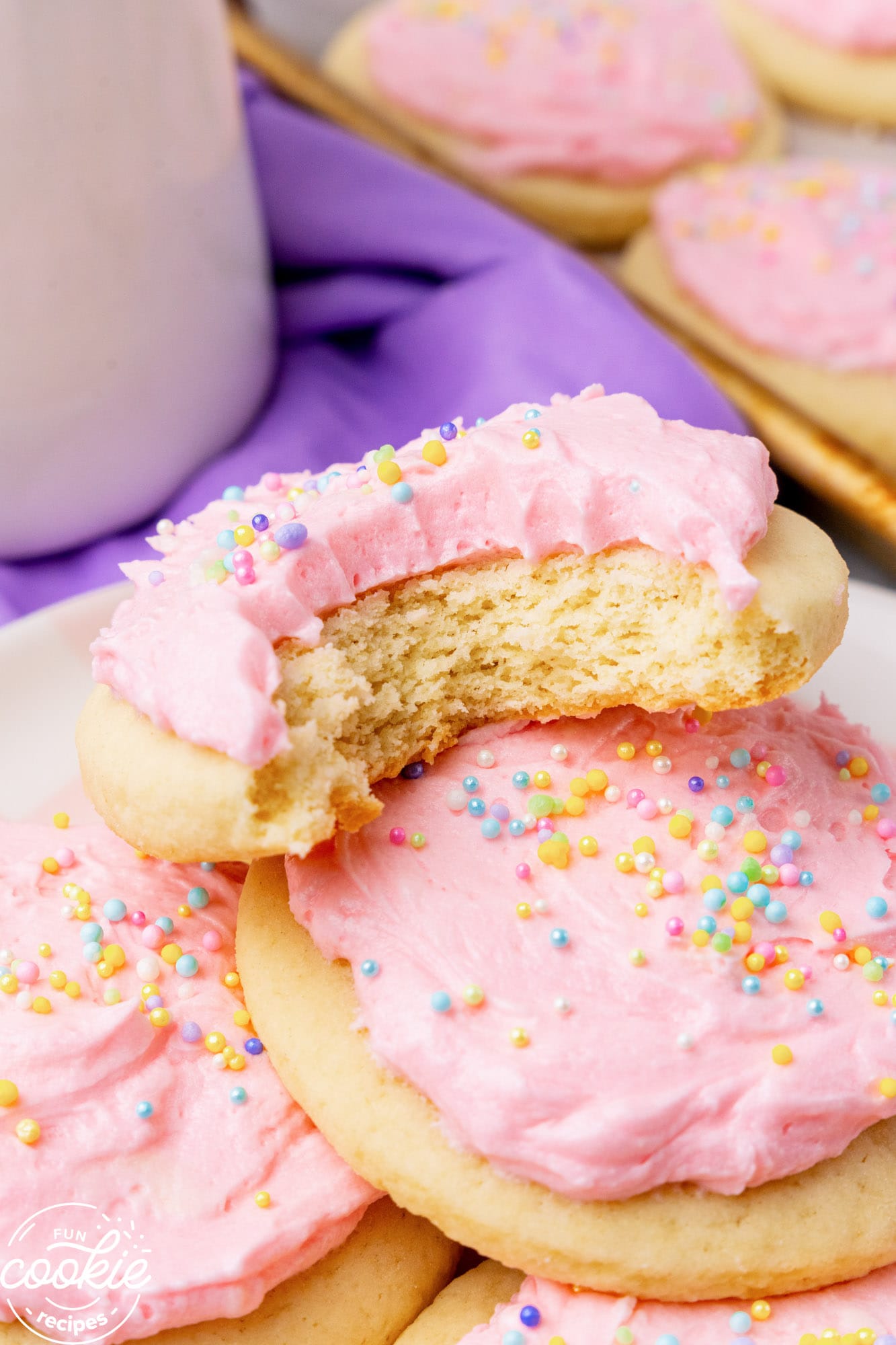 a plate of cookies with pink frosting. One has had a bite taken, to show the interior soft texture.