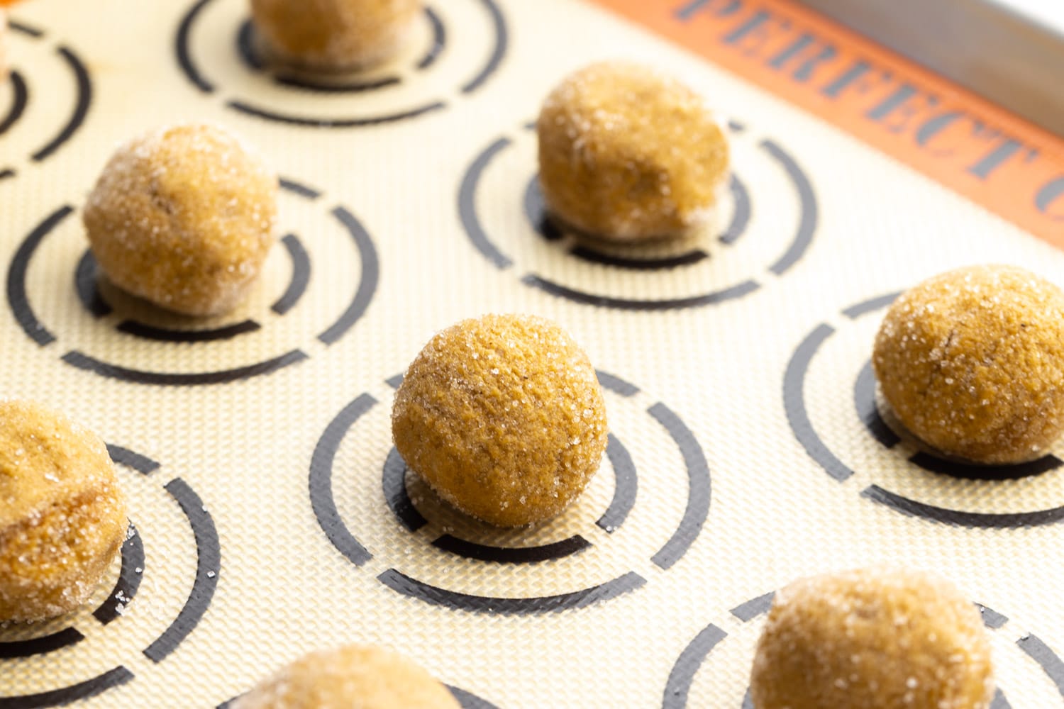Molasses cookie dough balls placed on a cookie sheet lined with a silicone mat