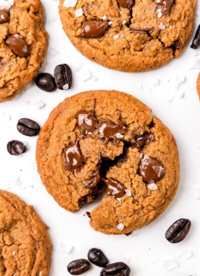 coffee cookies on a white counter. The cookies are filled with chocolate chips, and whole coffee beans are on the counter as well.