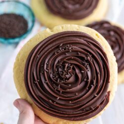 Holding a large cookie frosted with chocolate ganache frosting