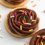 Round cut out sugar cookies decorated with chocolate frosting and rainbow sprinkles