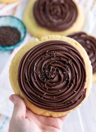 Holding a large cookie frosted with chocolate ganache frosting