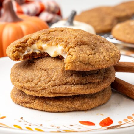 a plate of pumpkin cheesecake cookies. The top of the stack of three has a bite taken.