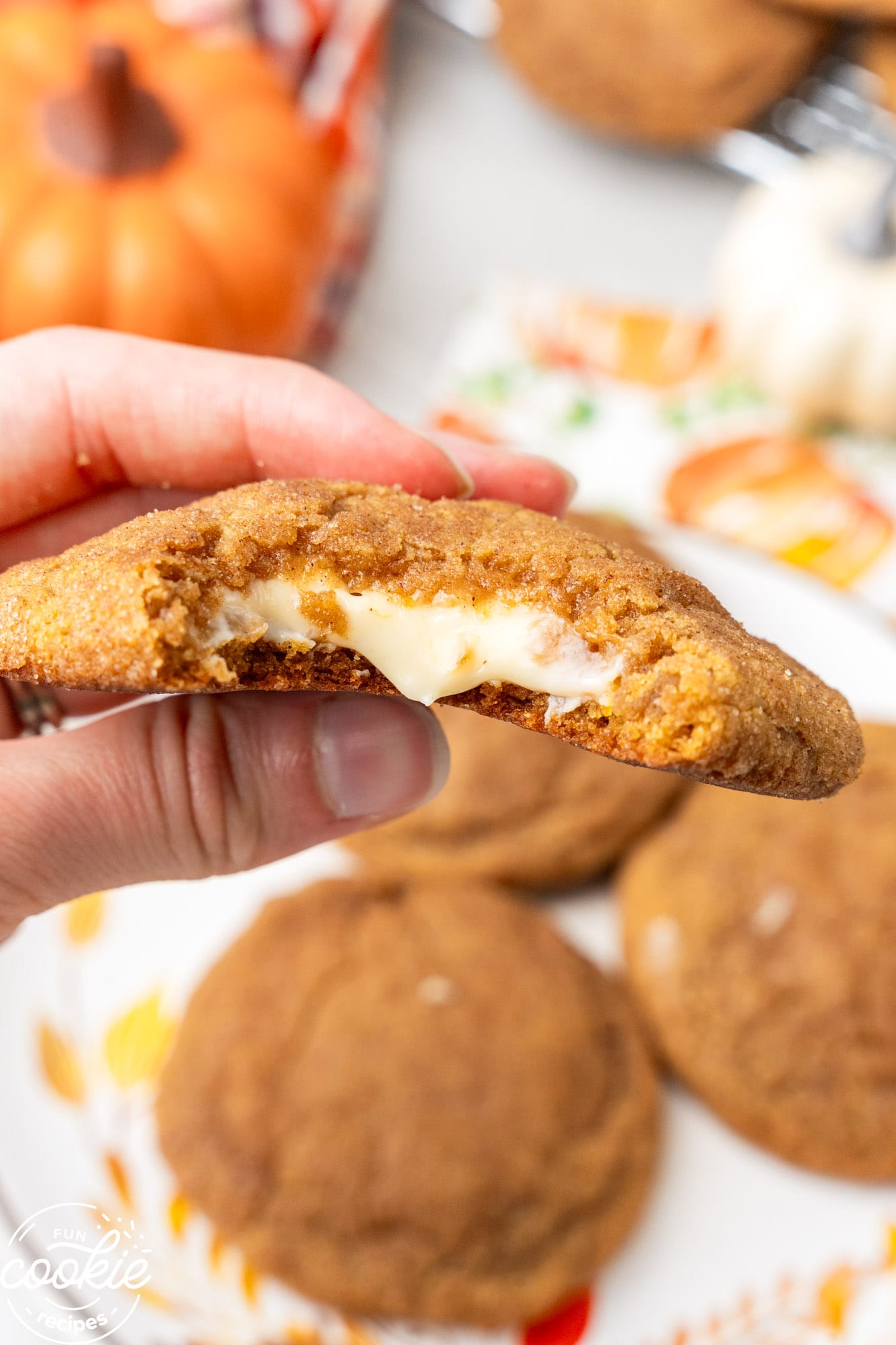 a hand holding a pumpkin cookie filled with a creamy cheesecake filling.