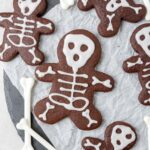 Overhead shot of halloween skeleton chocolate sugar cookies on a piece of parchment paper, with prop bones on the sides.
