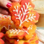 a stack of sugar cookies that look like fall leaves. a hand is holding one up to show the icing decorations.