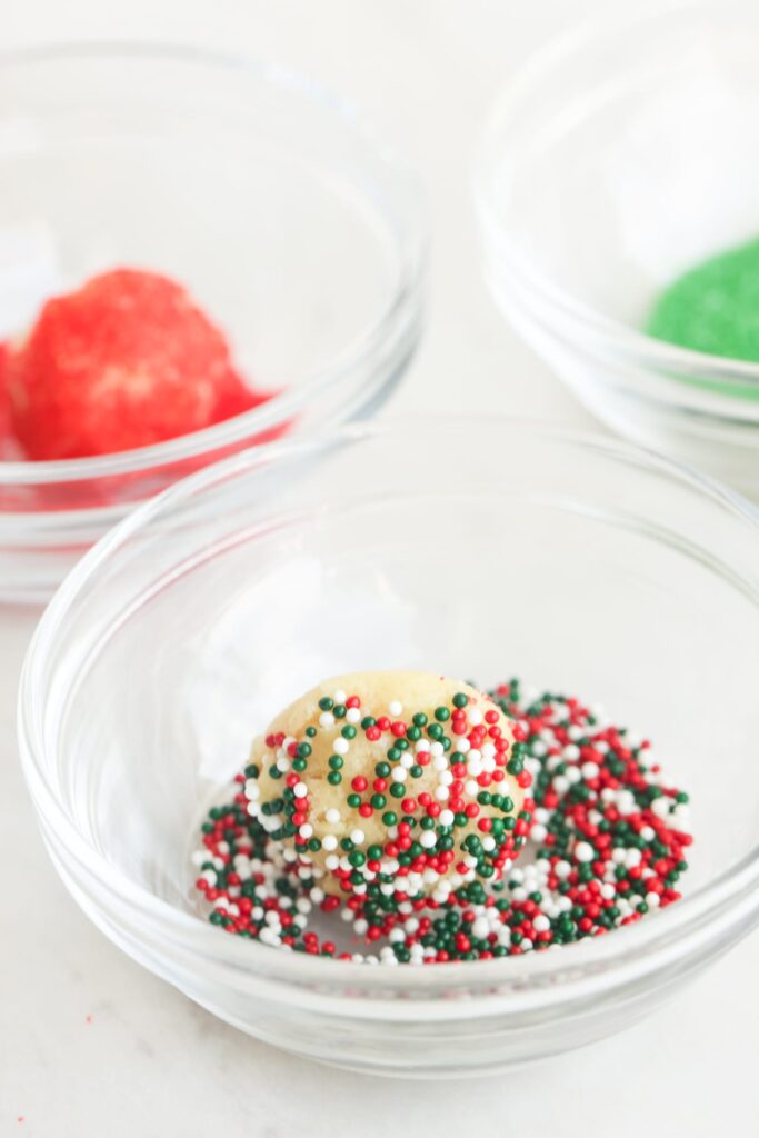 rolling sugar cookie dough into christmas sprinkles.