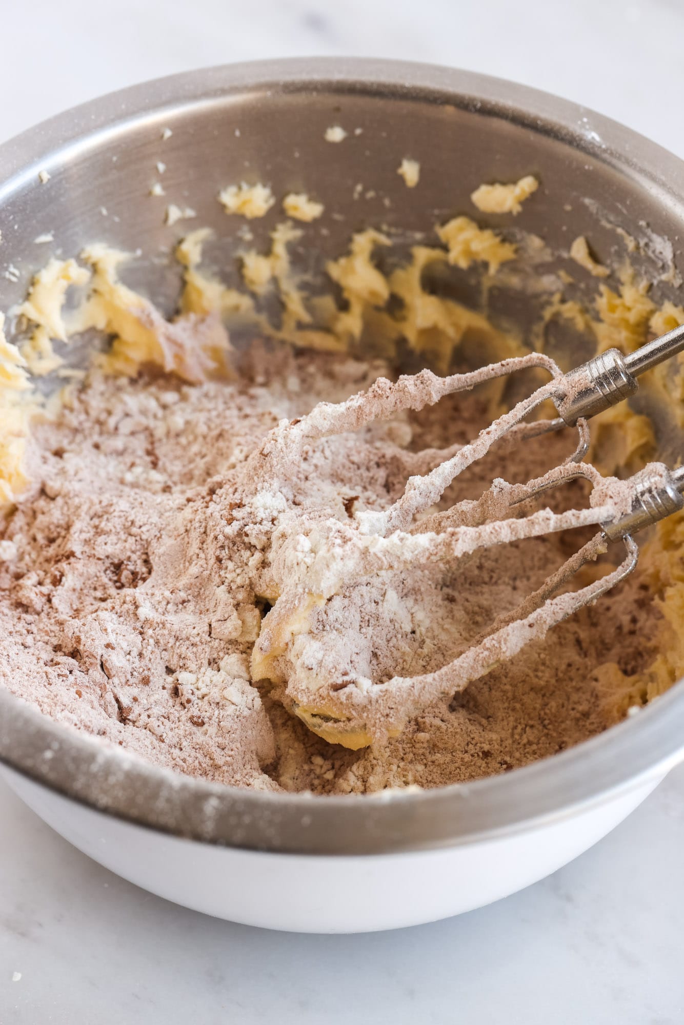In a mixing bowl, dry ingredients are added to creamed butter also shown mixer beaters on the side