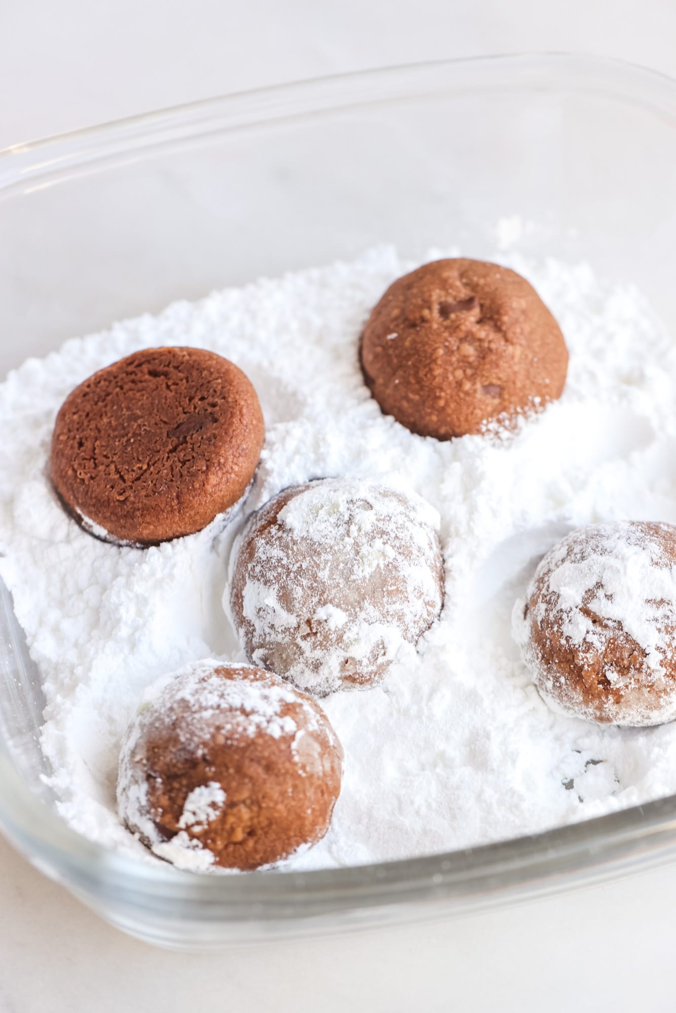 Chocolate, snowball cookies, being rolled in powdered sugar in a glass bowl