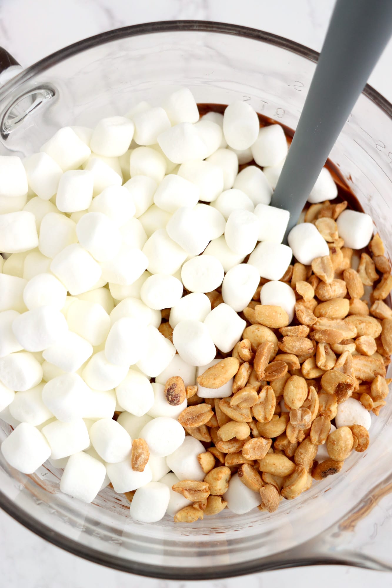 Marshmallows and roasted peanuts in a glass bowl with a spatula