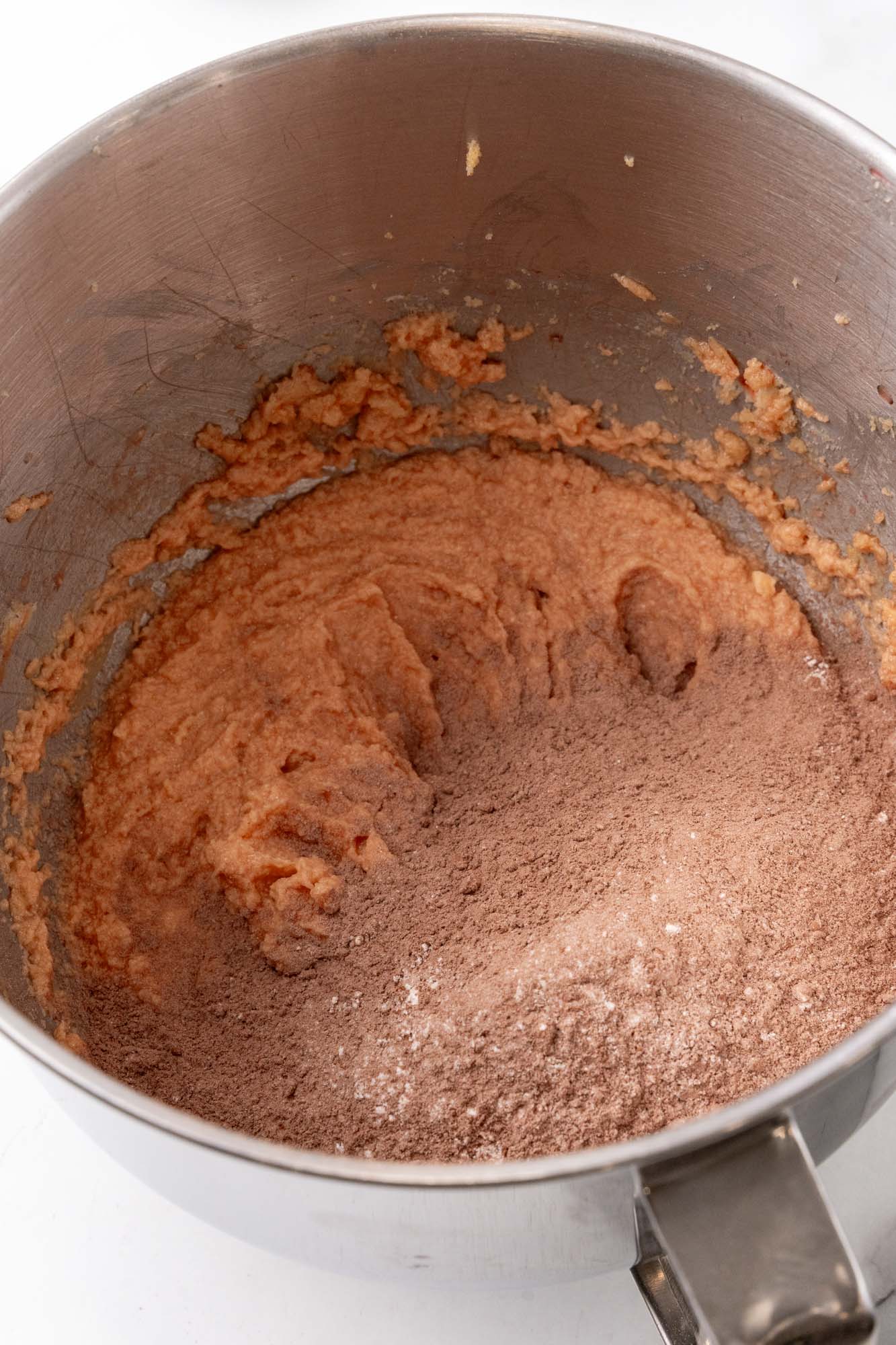 dry ingredients added to wet ingredients to make chocolate cookies, in a metal mixer bowl.