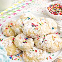 a white plate holding sprinkle funfetti cool whip cookies next to some colorful straws and a bowl of sprinkles.
