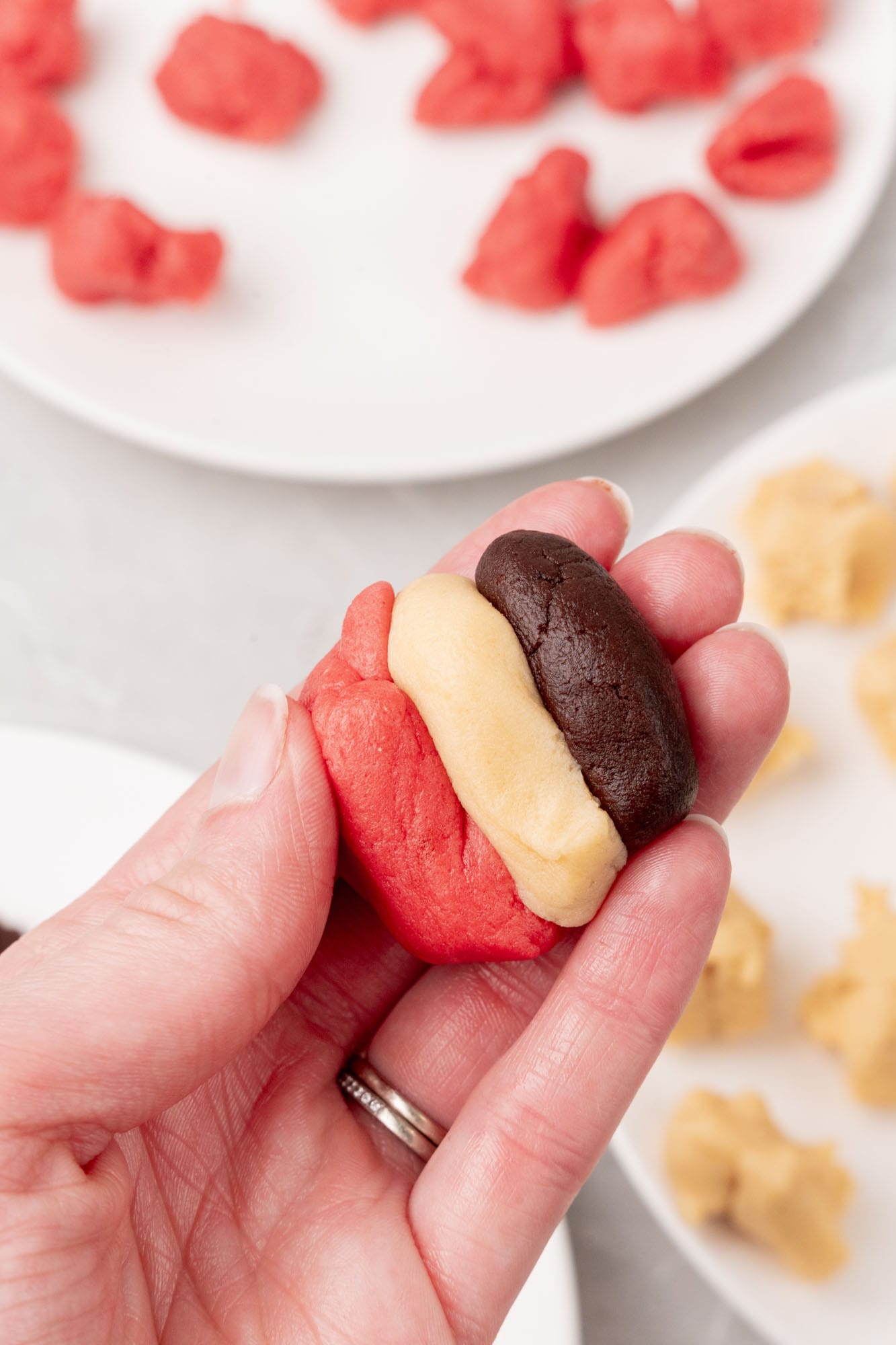 pink, white, and brown cookie dough pressed together to create a neapolitan cookie pattern in someone's hand.