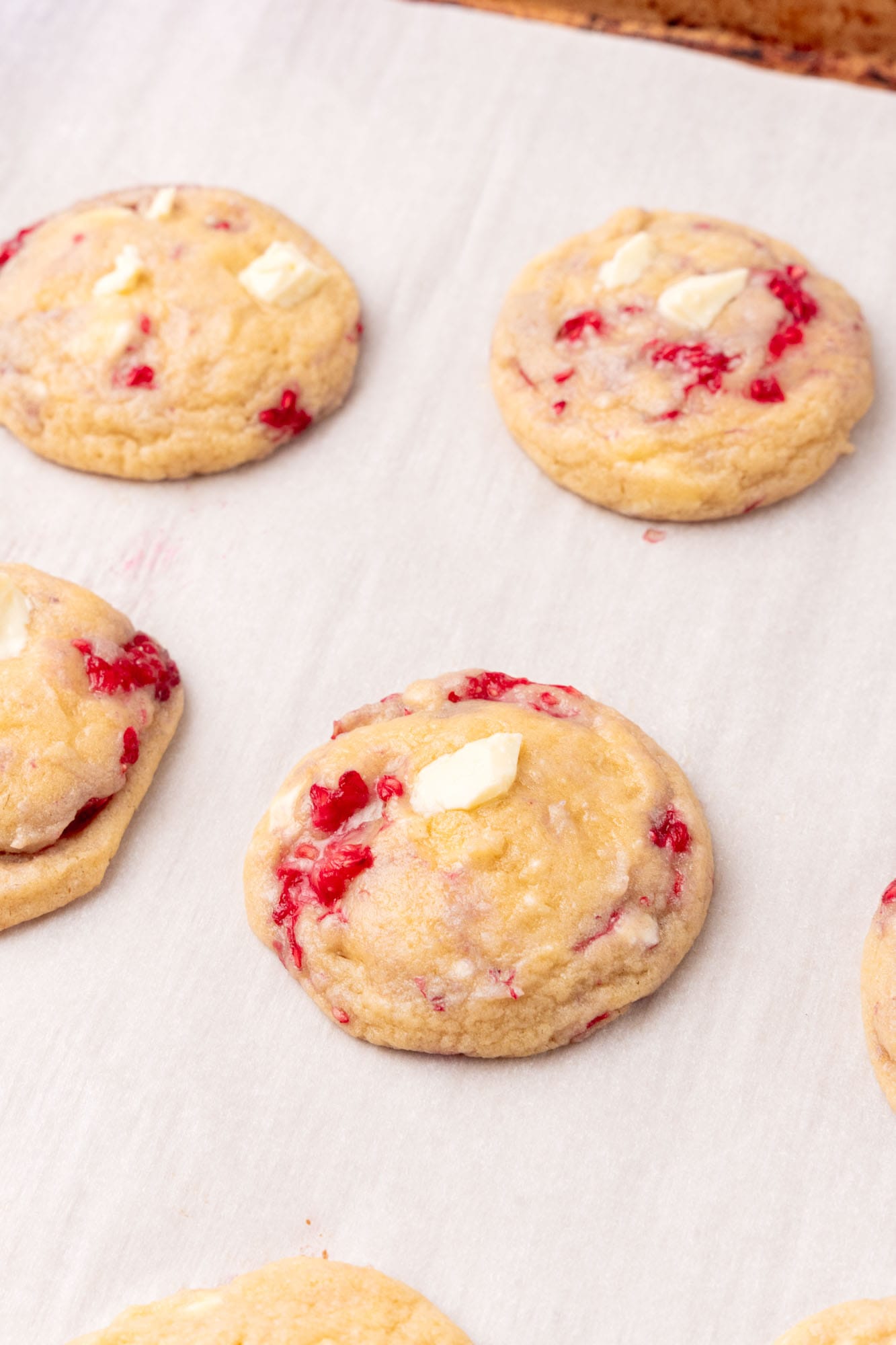 closeup of baked white chocolate chip and raspberry cookies on a parchment lined sheet.