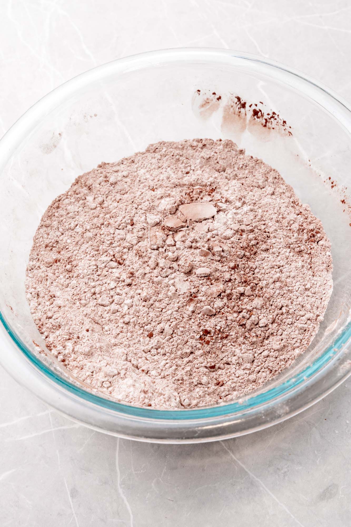 cocoa powder whisked into flour in a clear glass mixing bowl.
