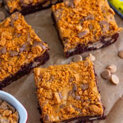 Four square butterfinger topped brownies on parchment paper.