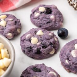 A countertop with purple blueberry cookies filled with white chocolate chips.