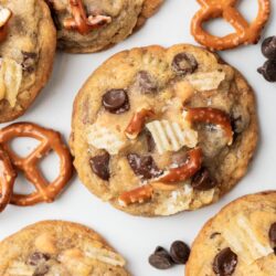 kitchen sink cookies on a white surface with chocolate chips and mini pretzels around.