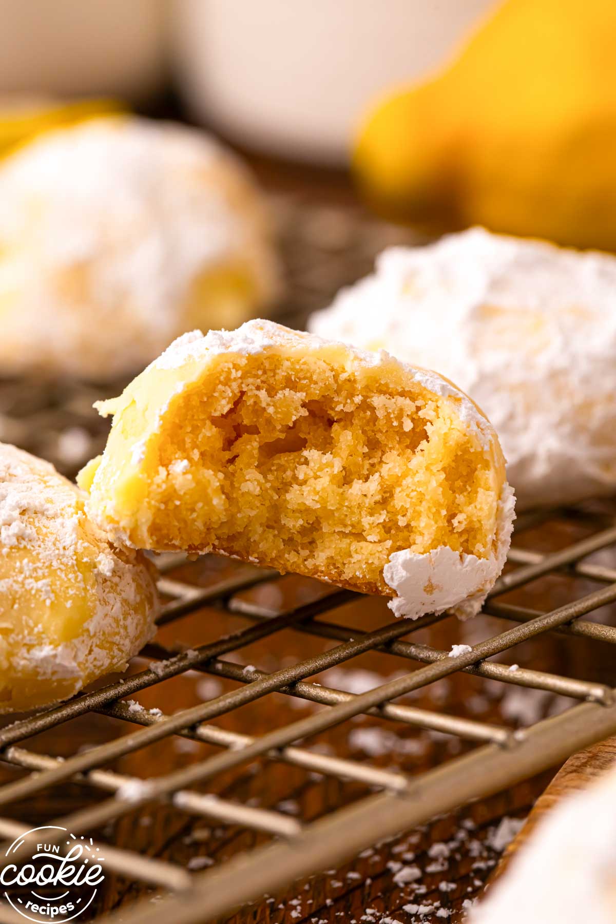 Close up of a lemon snowball cookie broken in half showing the soft, buttery interior and powdered sugar coating on a cooling rack