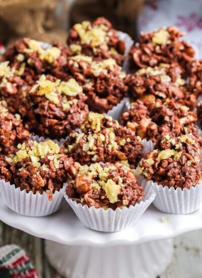 Chocolate potato chip clusters arranged on a white pedestal stand with festive holiday decorations in the background.