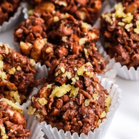 Close-up of a chocolate potato chip cluster topped with crushed chips with more clusters softly blurred behind it.