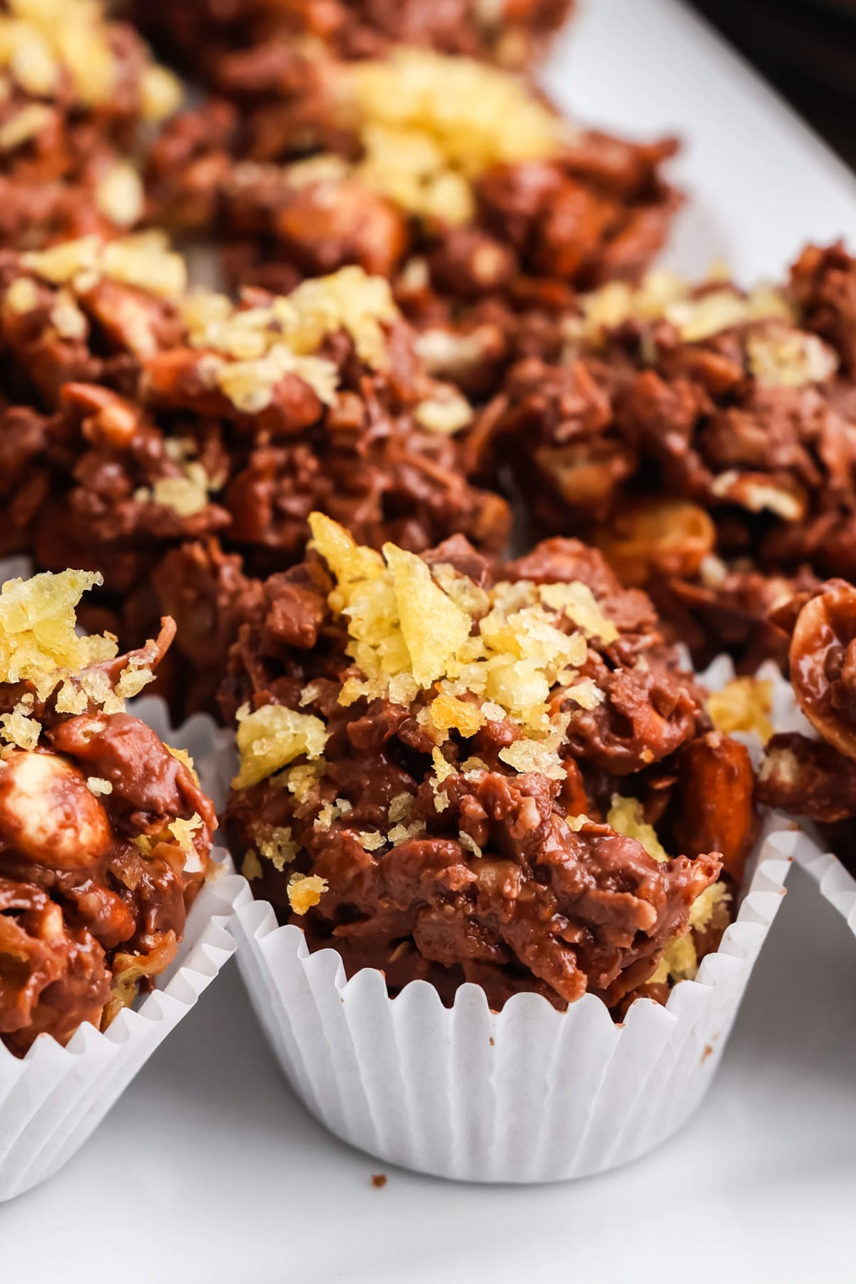 Detailed close-up of a chocolate potato chip cluster topped with crunchy crushed potato chips in a white liner.